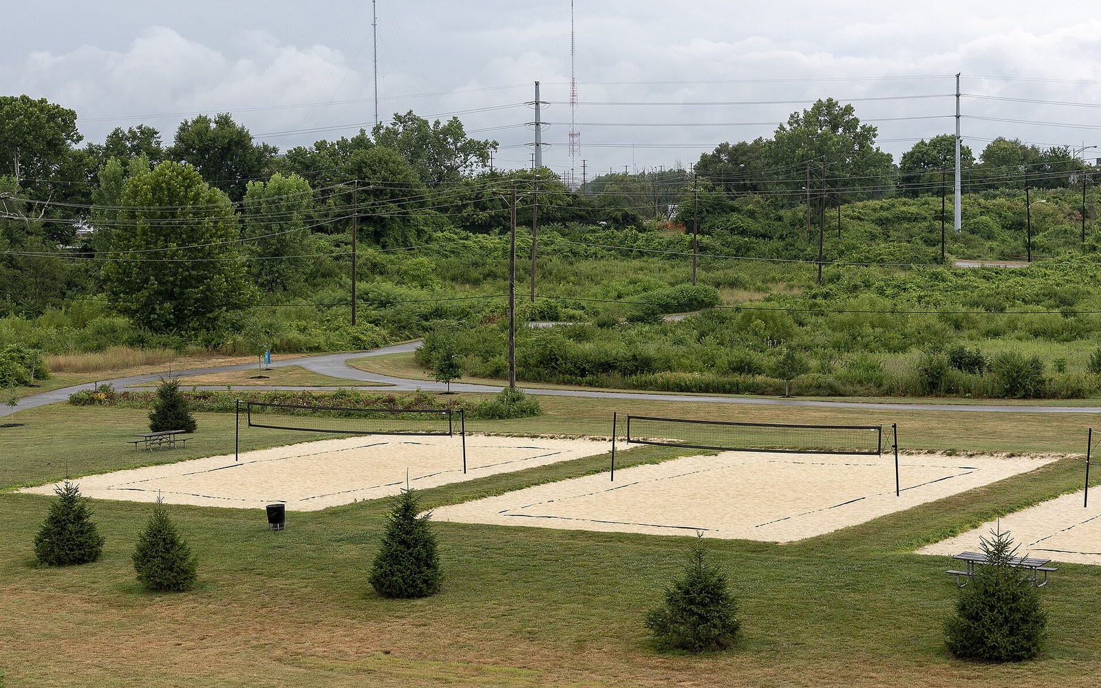 Empty sand volleyball courts with nets sit in a grassy park under power lines