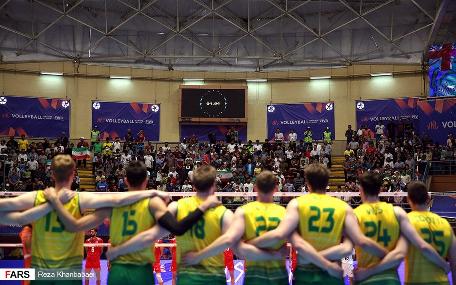 Volleyball players in yellow and green jerseys stand arm-in-arm facing the crowd before a match